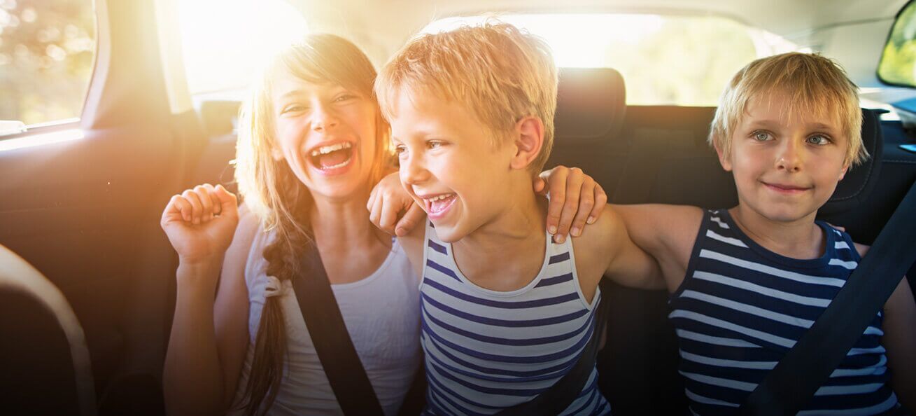 Drei lächelnde Kinder genießen ihren Roadtrip auf dem Rücksitz des Autos
